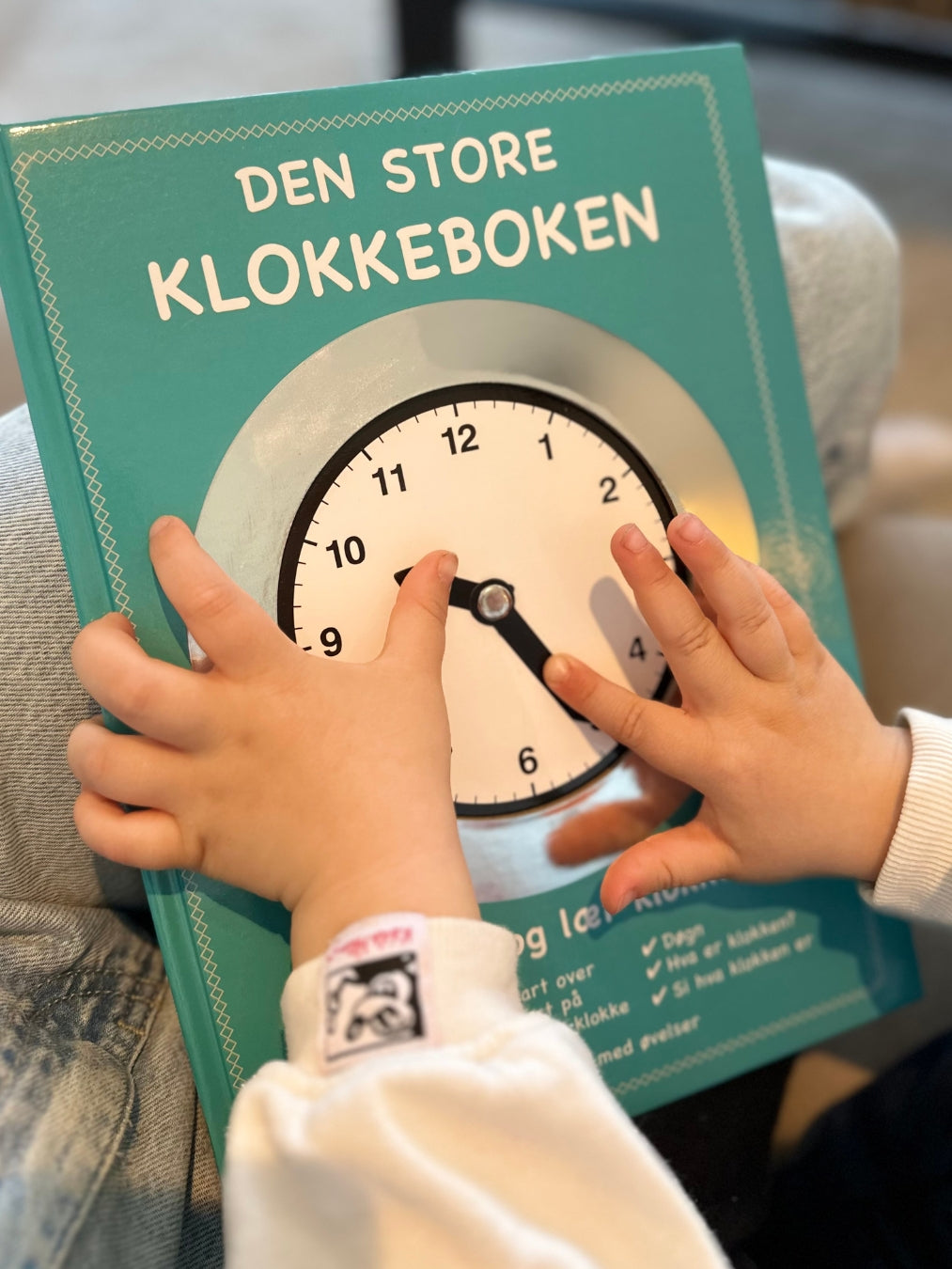 Nærbilde av et barn som øver på klokken. Bruke visere til å endre tiden. Lære klokken.