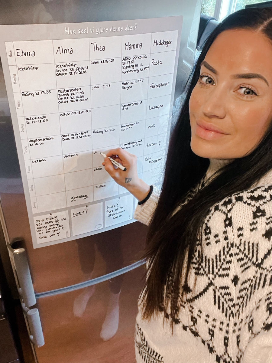 En trebarnsmamma som skriver på ukens aktiviteter på en ukeplanlegger.