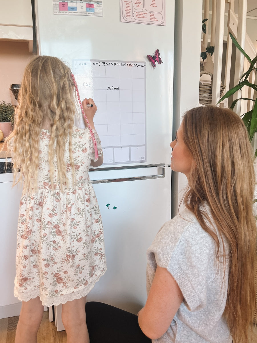 Magnetisk ukeplanlegger som blir fylt ut av mor og barn.